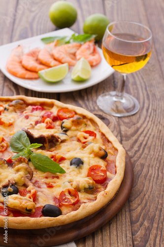 Big tasty pizza with seafood, tomatoes, wine on wooden table