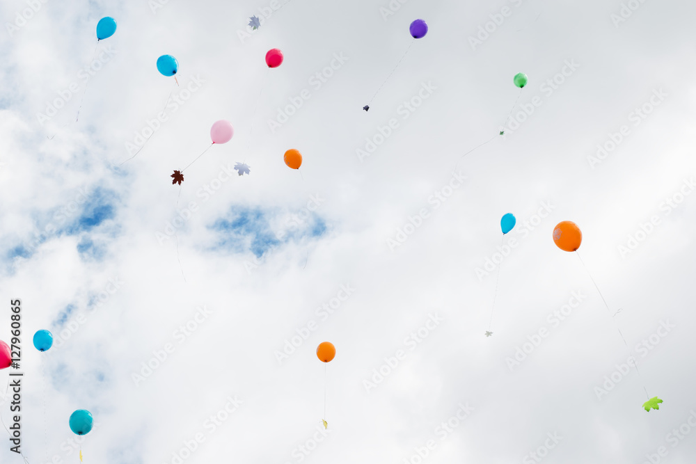 Multicolored balloons with maple leaves fly in the sky.