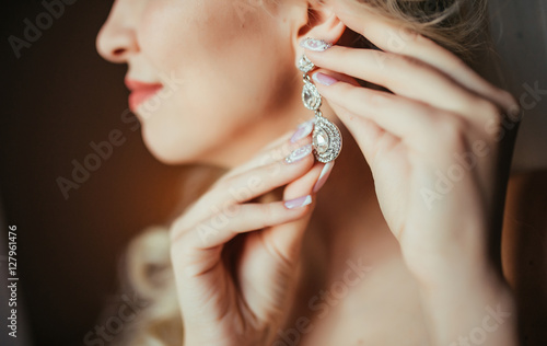 Wedding preparation. Beautiful, happy bride dresses earrings before wedding. Wedding accessories, jewelry. Closeup portrait of bride. Selective focus.