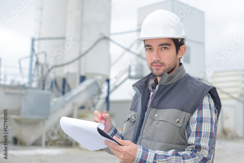young handsome foreman writing on his clipboard at construction site