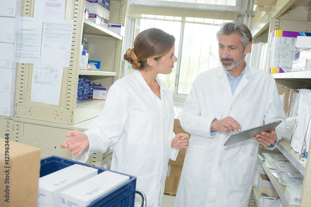 Obraz premium pharmacist dispensing medicine with teammate in the backoffice