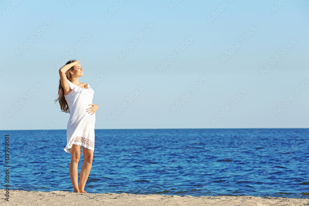 Young pregnant woman in white dress standing on the beach Young pregnant woman in white dress standing on the beach