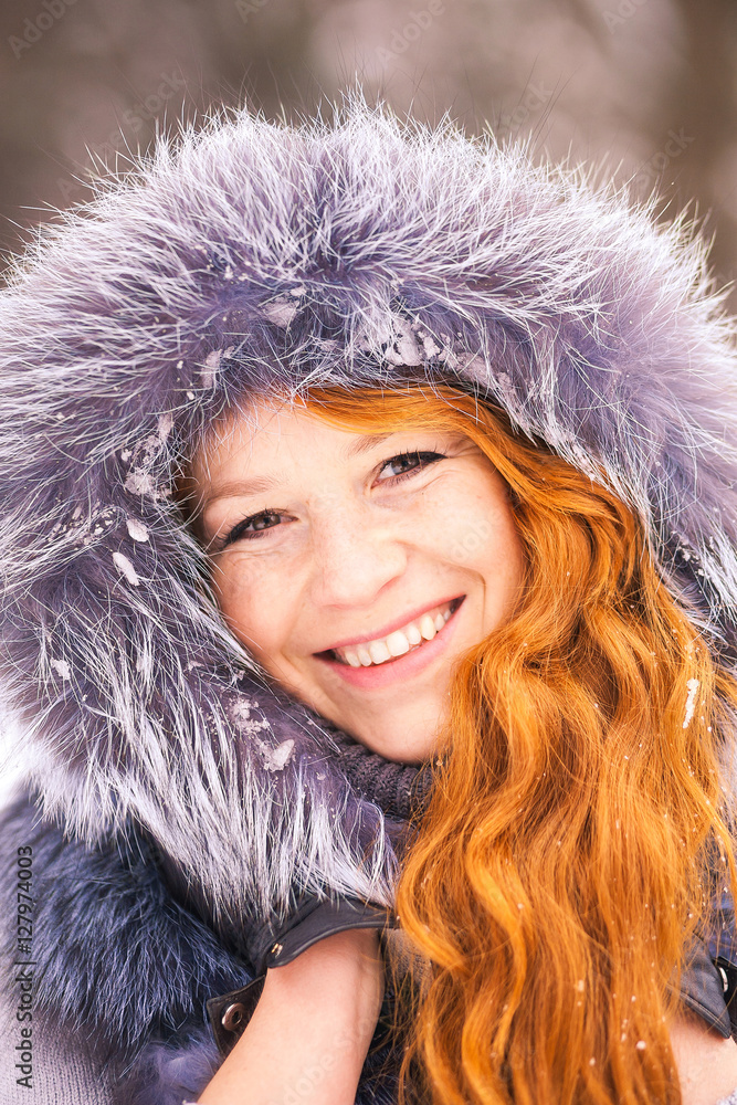 Portrait of beautiful young girl dressed in fur coat at winter trees background. Beauty woman having fun outside on snowy day. Close up of female smiling face with gorgeous long ginger hair. Portrait of beautiful young girl dressed in fur coat at winter trees background. Beauty woman having fun outside on snowy day. Close up of female smiling face with gorgeous long ginger hair.