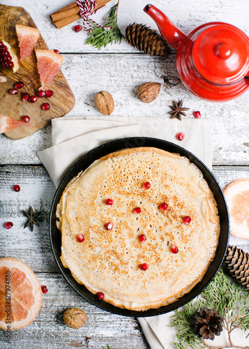 New Year pancakes on a wooden background with cones, cinnamon, pomegranate, red kettle and tea
