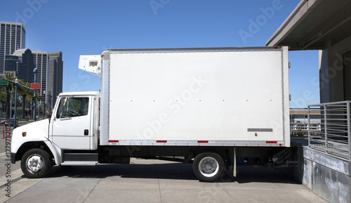 Parked refrigerated truck at loading dock under blue sky. Horizontal.