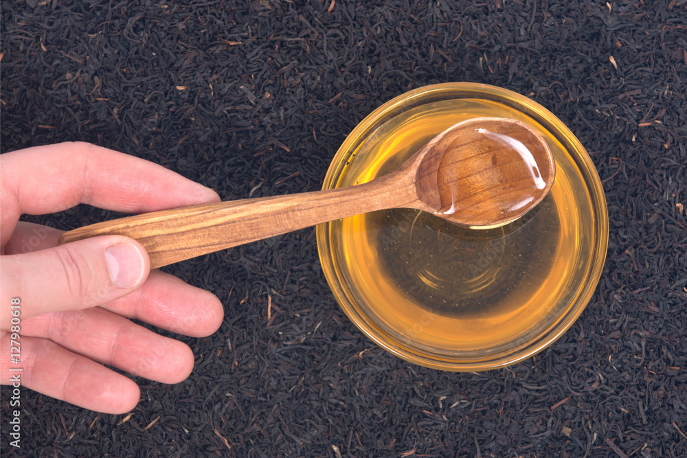 Organic amish farm pure honey in bowl and camellia assam tea with wooden spoon Organic amish farm pure honey in bowl and camellia assam tea with wooden spoon