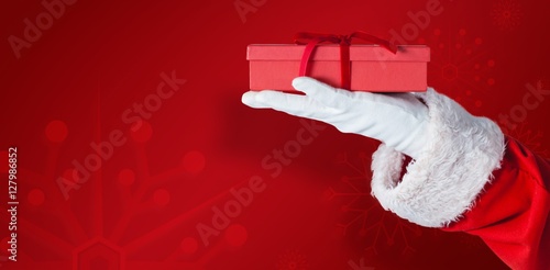 Composite image of santa claus holding gift box in hand