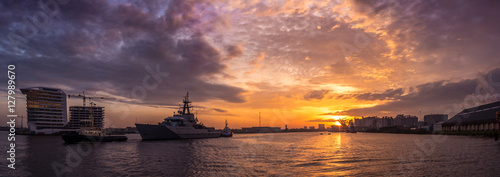British warship from the navy is leaving the port of Amsterdam with tugboat assistance. Beautiful panorama sundown background.
