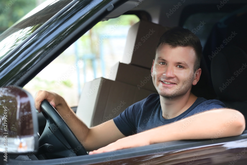 Young male deliverer with boxes sitting in car
