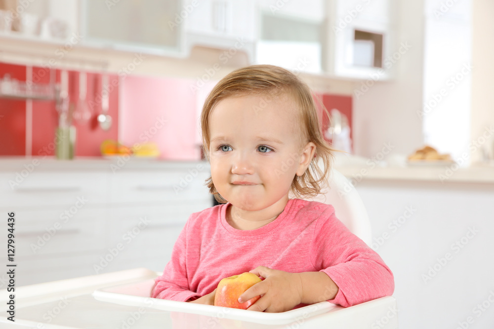 Cute little girl with apple in high chair at kitchen Cute little girl with apple in high chair at kitchen
