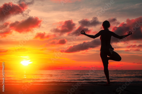 Silhouette young woman practicing yoga on the beach at surrealistic bloody red sunset.