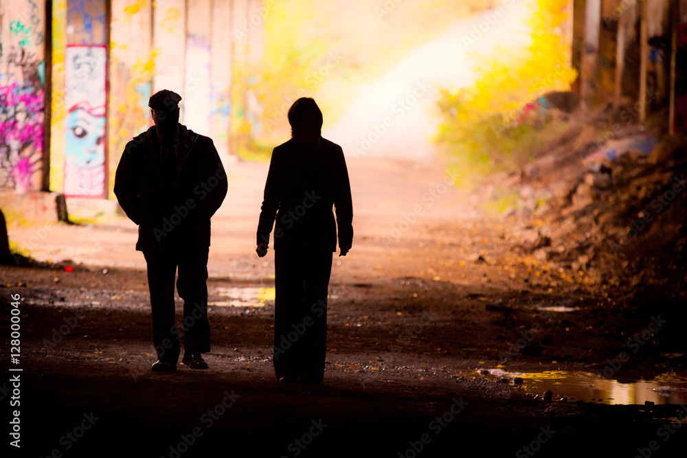 A silhouetted man and woman walk from an underground tunnel