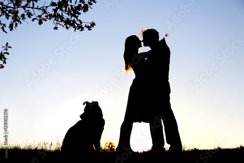 Silhouette of Loving Young Couple Hugging Under Tree at Sunset photo