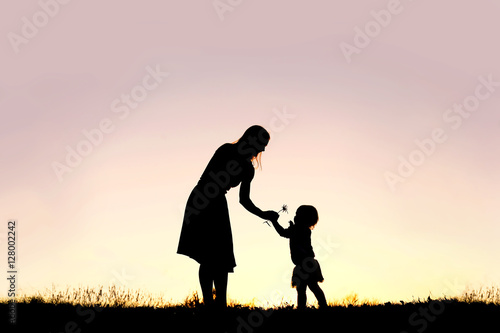 Silhouette of Baby Girl Giving Mom Flower at Sunset