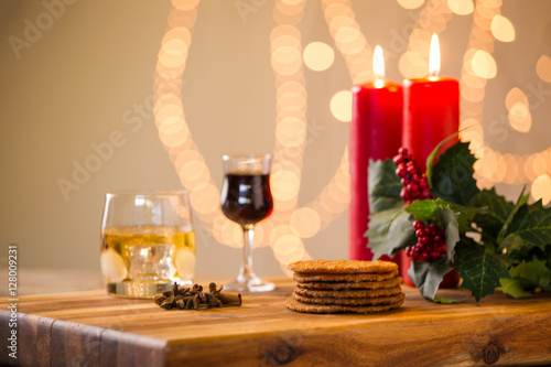 Lovely close up image of Christmas cookies on a wooden chopping board with some scented candles and a glass of whiskey / coffee and some cinnamon sticks.