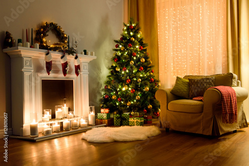 A cozy living room lighted with numerous lights decorated ready to celebrate Christmas. Christmas room interior design, Xmas tree decorated by lights, candles and garland lighting indoors fireplace.