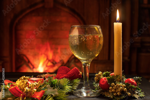 Christmas card, a glass of champagne and Christmas candle on the background of the fireplace
