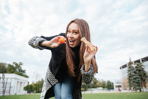 Happy lovely young woman showing bone and ball for dog