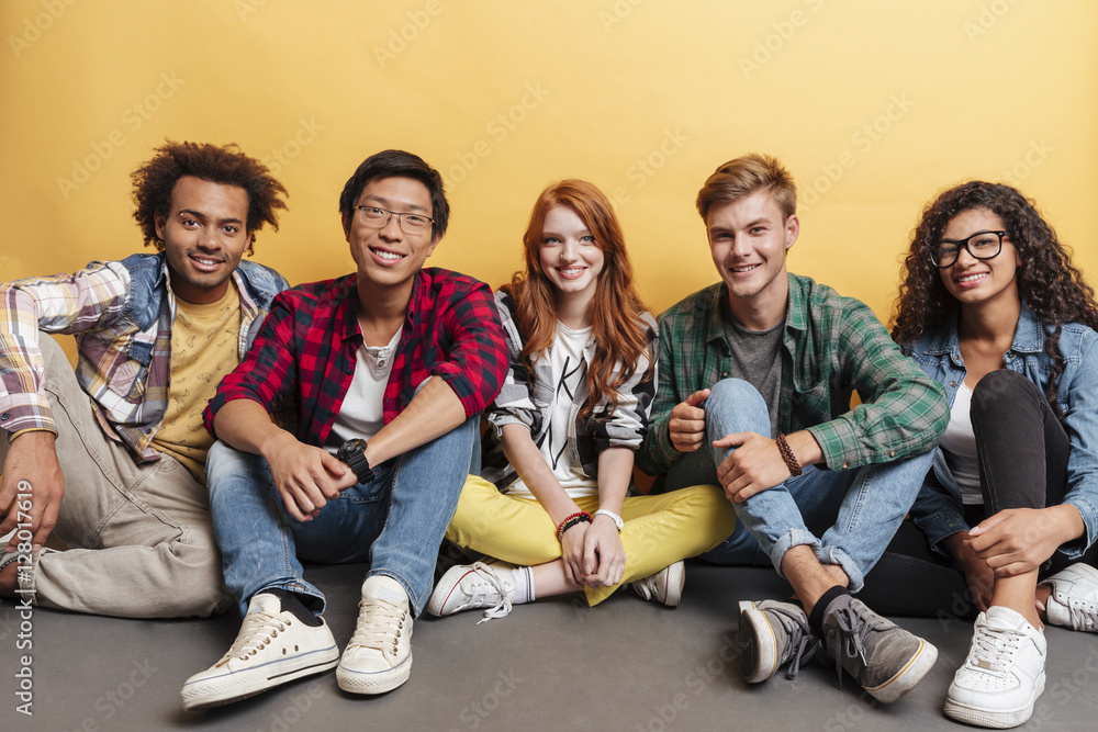 Multiethnic group of smiling friends sitting on the floor together - obrazy, fototapety, plakaty 