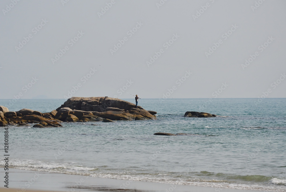 man fishing on rock at beach