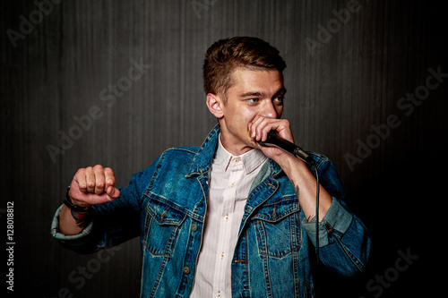 Young Guy in Jeans Jacket Beat Boxing with Microphone in Studio. Singer Beatboxing Performance. Concert and Beat Box Music Concept. Dark Background. Toned Photo.