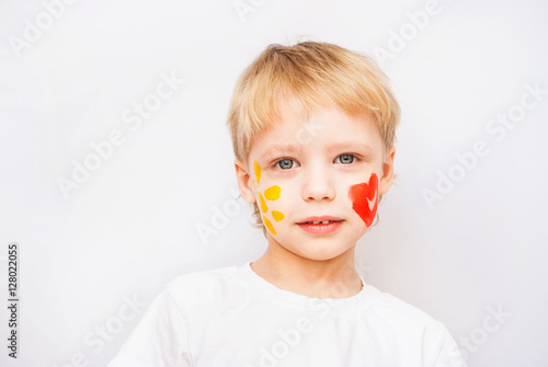 Portrait of funny beautiful blond child isolated on white background. Read heart and yellow sun on cheeks of boy.