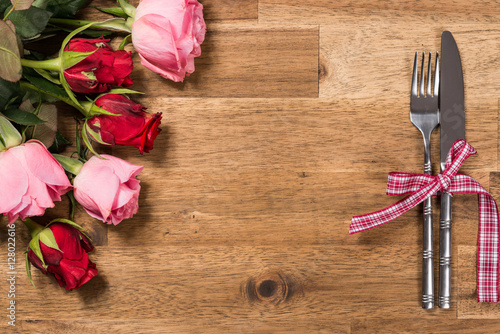 Wooden table with roses, knife and fork. Valentines day background