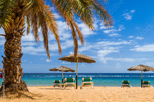 Fototapeta Naklejka Na Ścianę i Meble -  Deck chairs under umbrellas and palm trees on a tropical beach