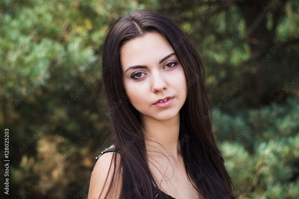 Graceful charming brunette model posing in black dress in coniferous park Graceful charming brunette model posing in black dress in coniferous park