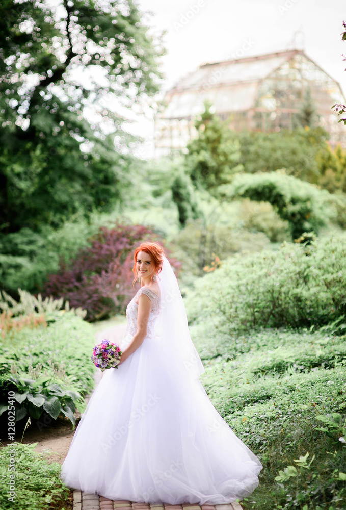 happy and young bride in white dress standing in the garden