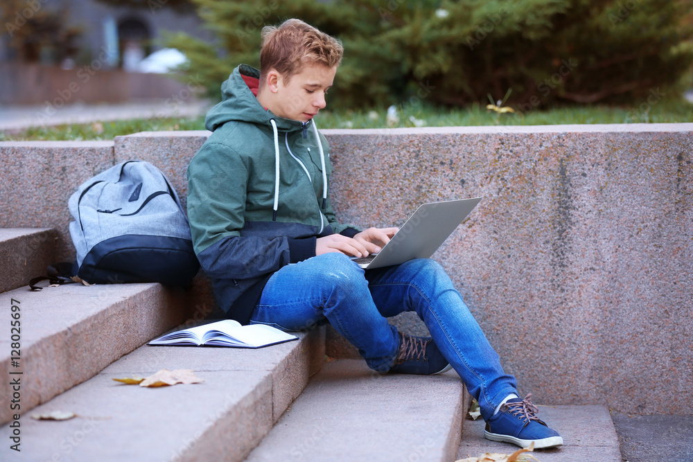 Teenager with laptop sitting on steps outdoors