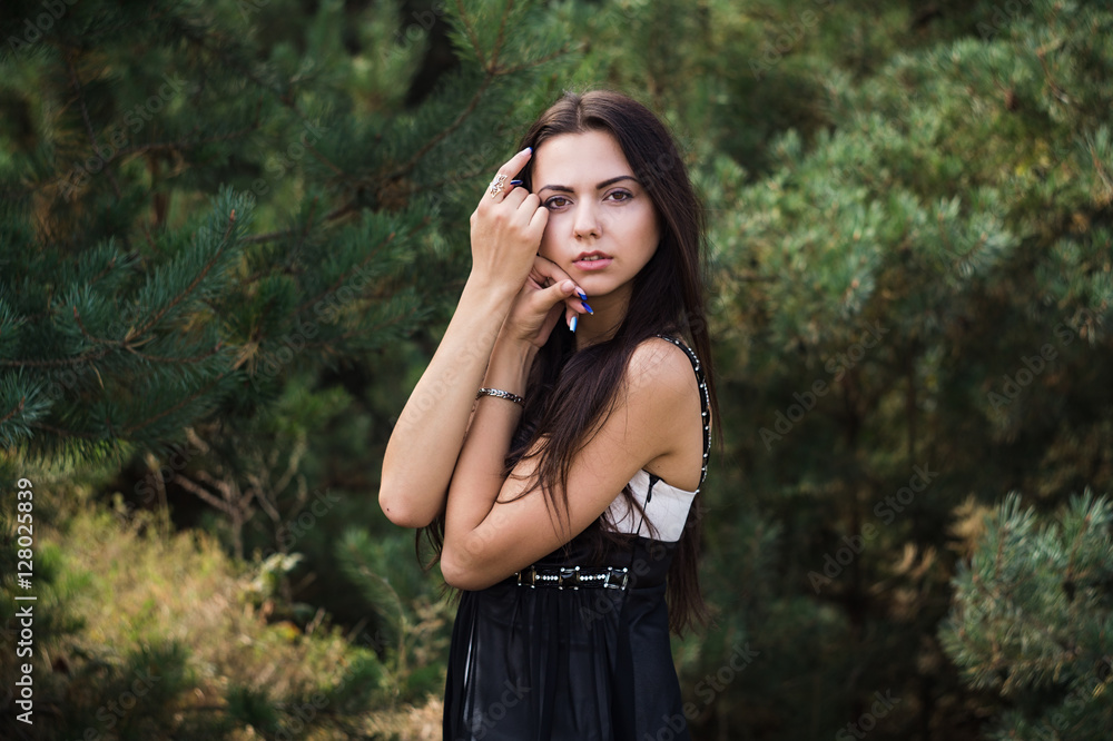 Graceful charming brunette model posing in black dress in coniferous park Graceful charming brunette model posing in black dress in coniferous park