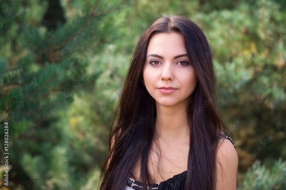 Naklejka premium Graceful charming brunette model posing in black dress in coniferous park