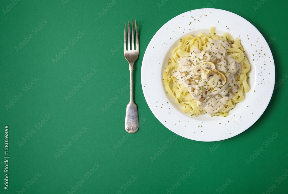 A dinner dish full of tagliatelle spaghetti with a creamy mushroom pasta sauce, on a green background with fork and blank space at side