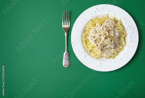 A dinner dish full of tagliatelle spaghetti with a creamy mushroom pasta sauce, on a green background with fork and blank space at side