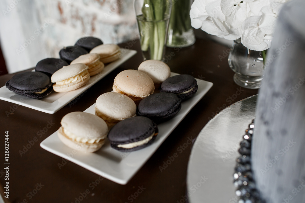 Black and white macaroons stand on square plates before white bo Black and white macaroons stand on square plates before white bo