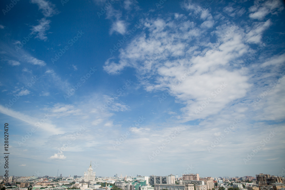 Blue sky with light white clouds hangs over grey city