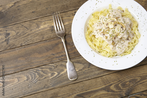 A dinner dish full of tagliatelle spaghetti with a creamy mushroom pasta sauce, on a rustic wooden table background with fork and blank space at side