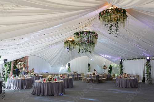 Chandeliers made of roses and greenery hang under the white tent photo