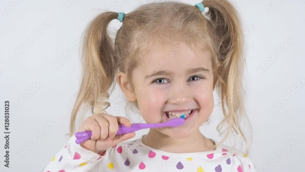 Cute little girl with pigtails diligently brushing his teeth. In the hand of the girl has toothbrush. Cheerful girl looking into the camera. Cute little girl with pigtails diligently brushing his teeth. In the hand of the girl has toothbrush. Cheerful girl looking into the camera.