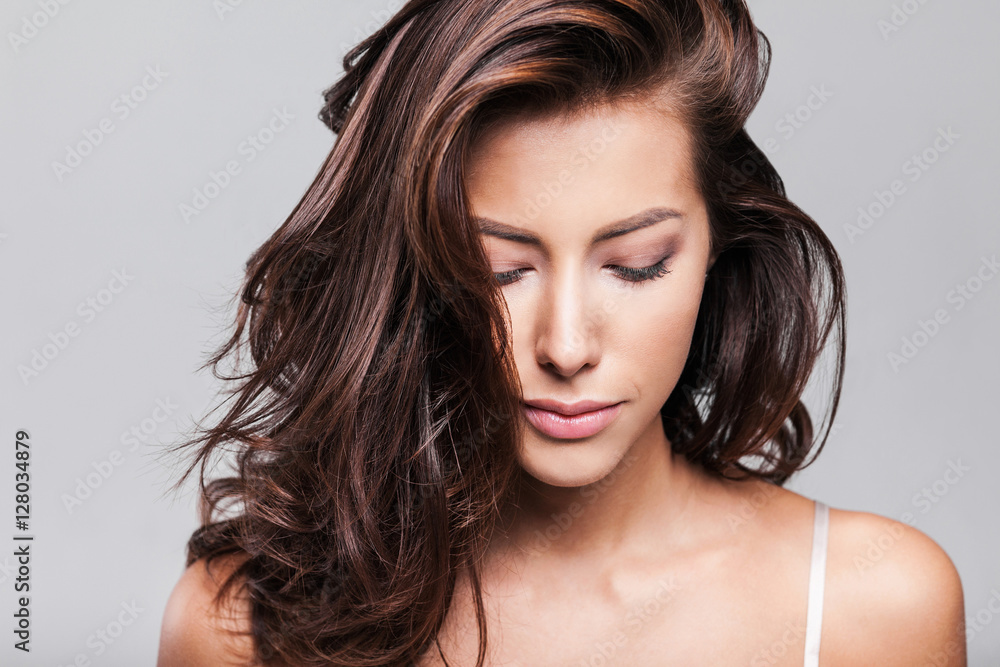 Naklejka premium Studio portrait of a beautiful young woman with long brunette hair. Pretty spa model girl with perfect fresh clean skin. Youth and skin care concept