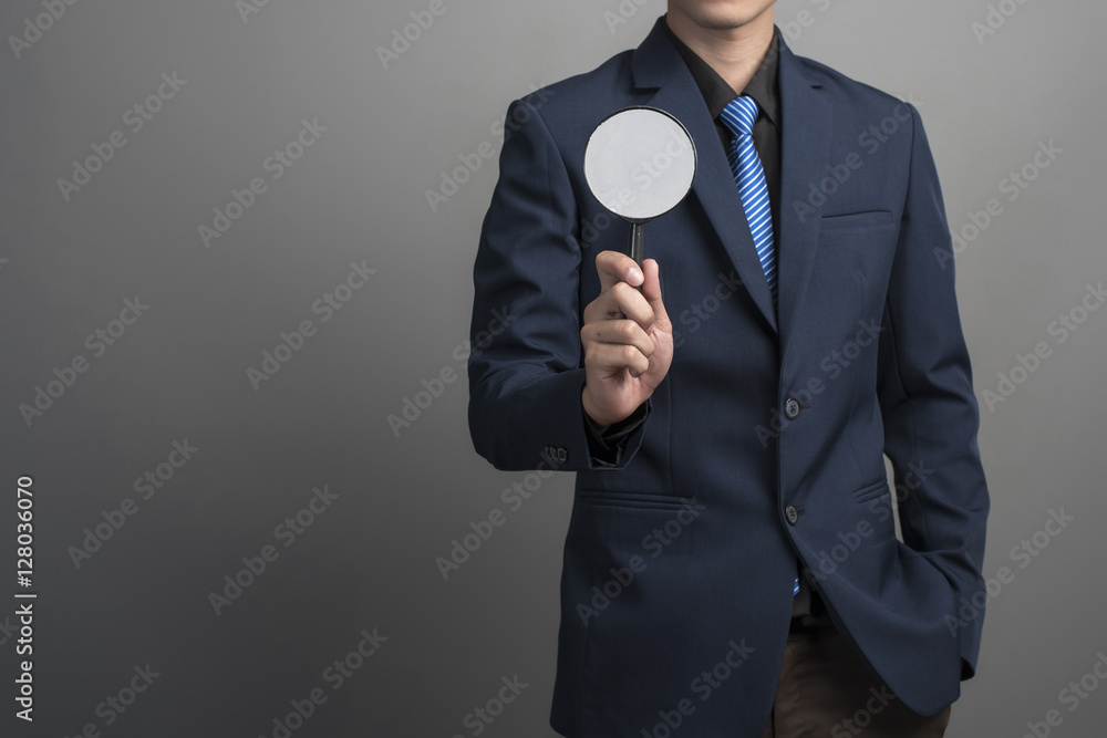 Close up of businessman in blue suit holding magnifier on gray b Close up of businessman in blue suit holding magnifier on gray b