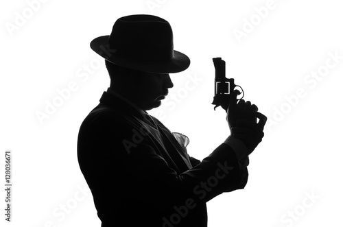 Silhouette of private detective with a gun in right hand. Agent stay side to camera and looks like mafioso Al Capone. Criminal scene. Studio shot