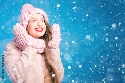 Winter portrait of a beautiful woman in knitted pink scurf, gloves and hat with snow flake on the blue background