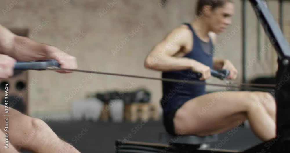 Fit man and woman exercising in gym, working out on rowing machine Fit man and woman exercising in gym, working out on rowing machine