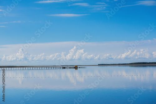 Blue sky reflected in a calm lake. White clouds reflected in a lake. Clouds hang low over the lake.