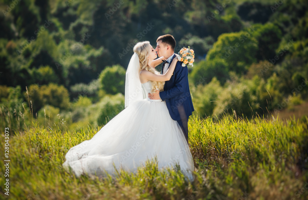 Young couple in love, groom and bride in wedding dress kissing at the nature. Wedding. Wedding day. Bridal bouquet.