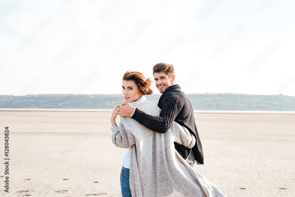 Back view of a young casual couple walking along beach
