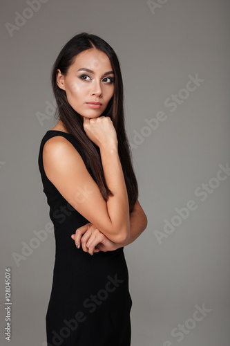 Pensive young woman in black dress standing and looking away