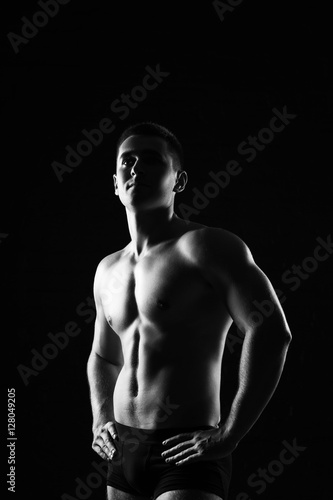 Male fitness model showing muscles in studio with a black backgr